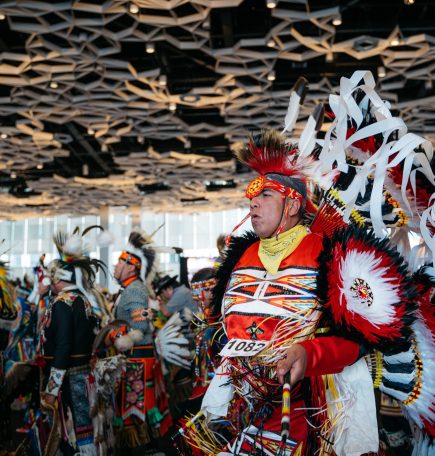 Une personne autochtone vêtue d'une coiffe traditionnelle danse avec d'autres personnes lors du pow-wow du festival Manito Ahbee.