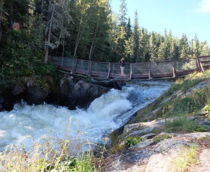 Une personne debout sur le pont suspendu dans le parc provincial Wekusko Falls, regardant l'eau se précipiter.