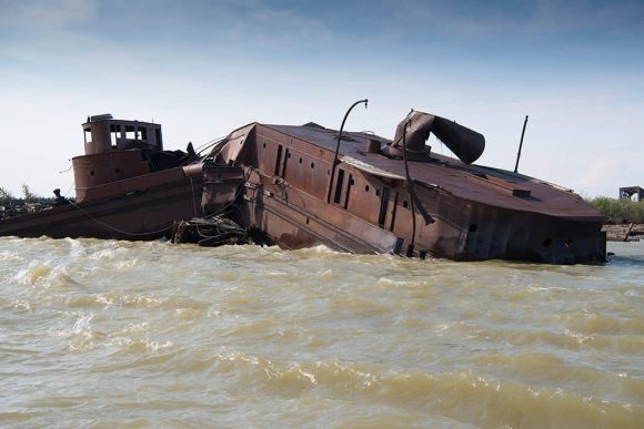 Bateau rustique de traite des fourrures partiellement submergé au bord de l'eau, présentant une dégradation naturelle et une importance historique.