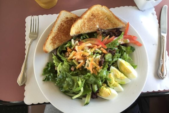 Salade fraîche garnie de fromage, servie avec du pain grillé et des œufs durs coupés en quatre pour un repas nutritif.