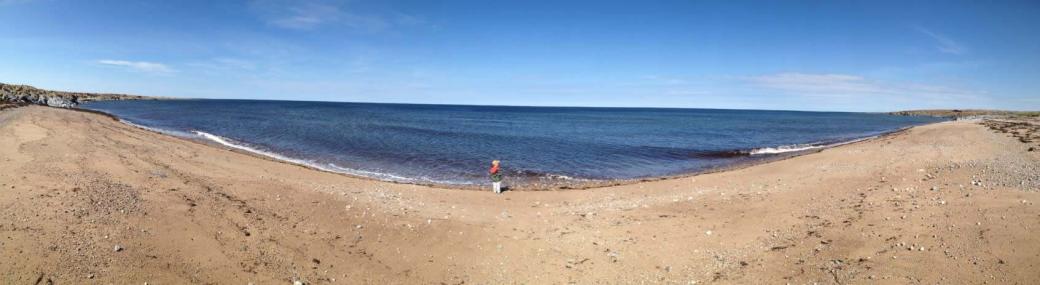 Enfant jouant au bord de l'eau sur une plage de sable, capturé au téléobjectif, soulignant la joie de l'été.