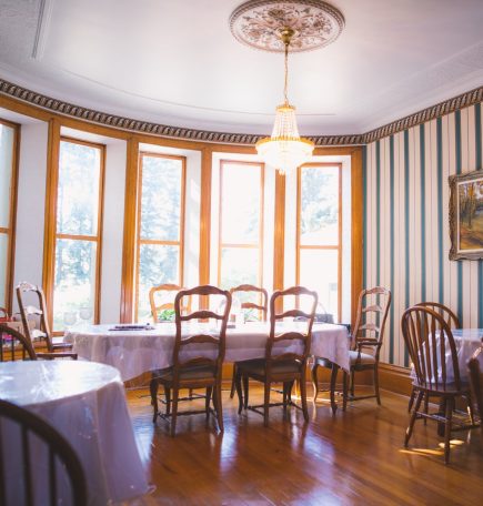 Une salle à manger lumineuse avec de nombreuses fenêtres et des planchers en bois dur, abritant quatre tables recouvertes de nappes et de chaises blanches.