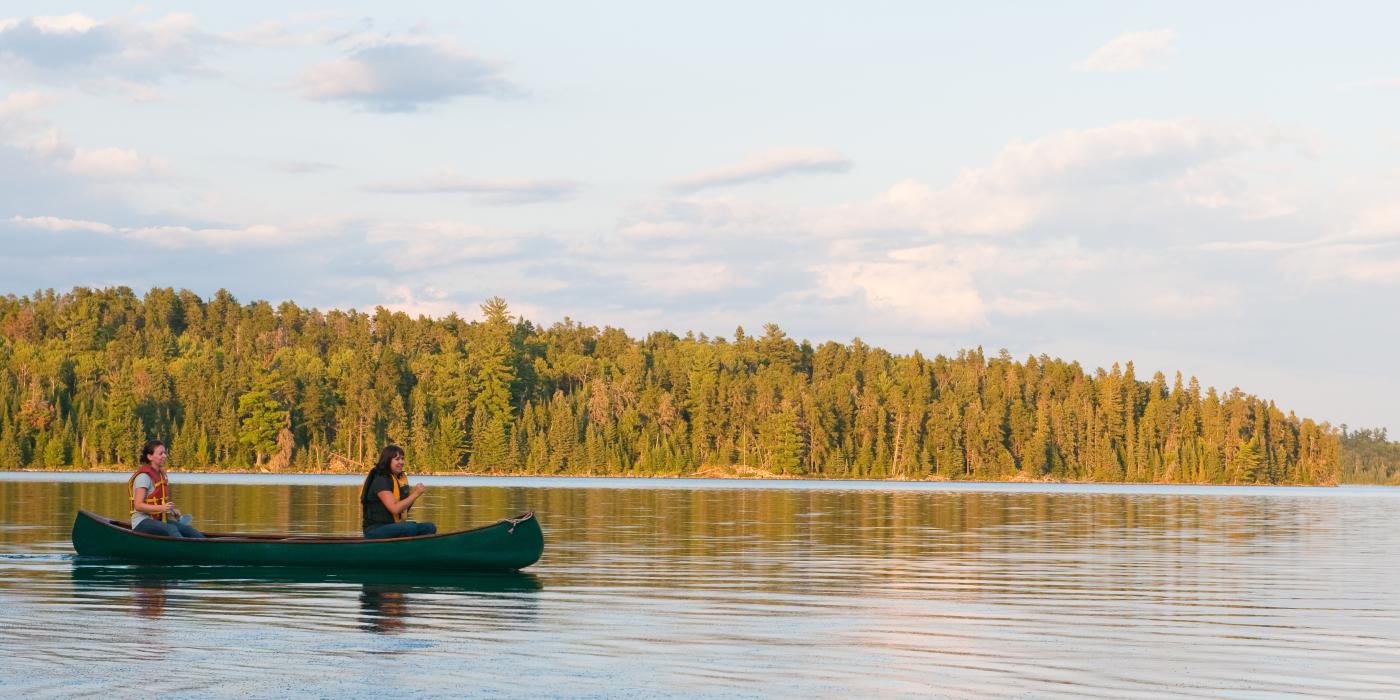 Deux femmes dans un canoë vert sur un lac avec une forêt en arrière-plan