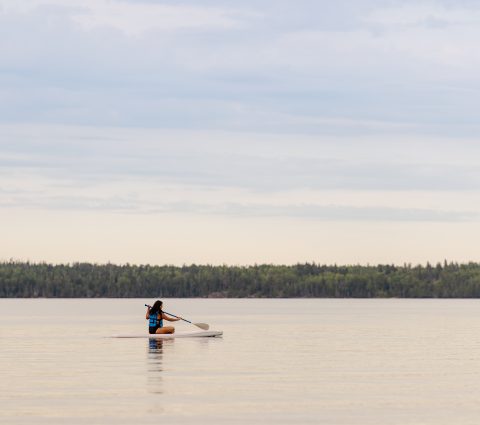 Une femme s'assoit et fait du paddleboard sur un lac.